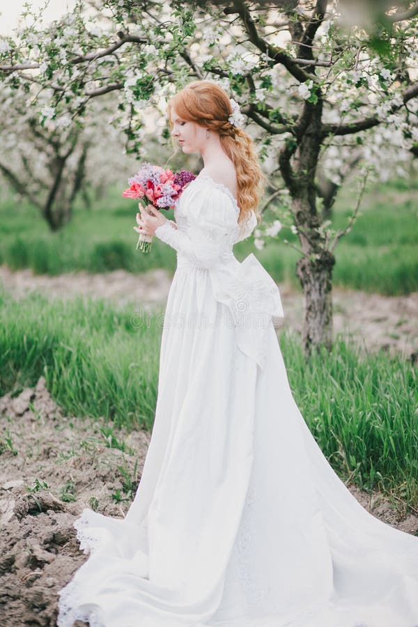 Beautiful bride in a vintage wedding dress posing in a blooming apple garden. Spring mood. Young woman in a white vintage dress