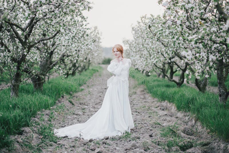 Beautiful bride in a vintage wedding dress posing in a blooming apple garden. Spring mood. Young woman in a white vintage dress