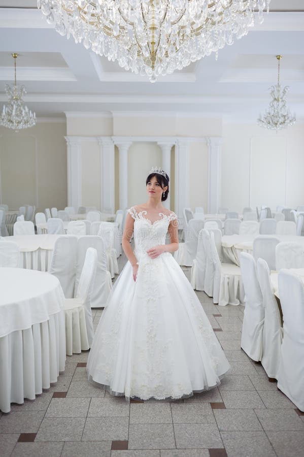 Beautiful bride in a wedding dress in a luxurious white room with a large chandelier