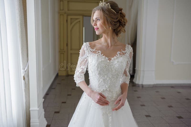 Beautiful bride in a wedding dress in a luxurious white room with a large chandelier