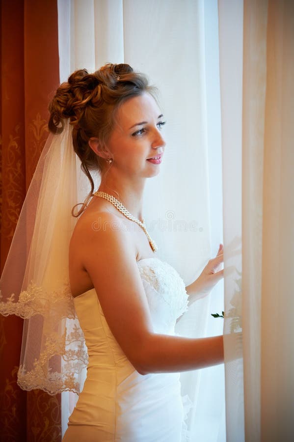 Beautiful bride in wedding dress near window