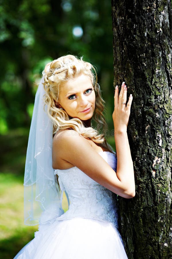 Beautiful bride in wedding dress stands near tree