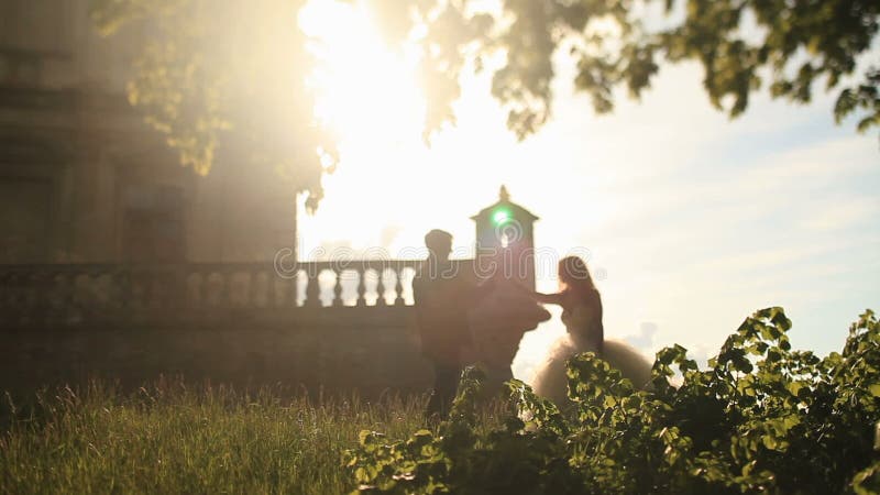 Beautiful bride in white gown holding hand of handsome groom near romantic vintage palace in warm sunset rays stock video footage Beautiful bride in white gown holding hand of handsome groom near romantic vintage palace in warm sunset rays stock video footage