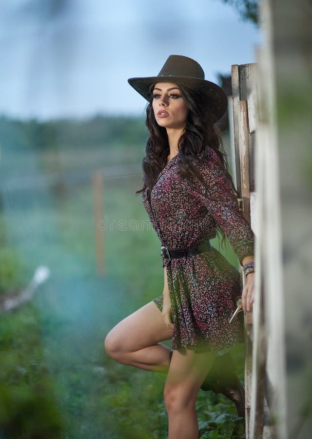 Beautiful brunette girl with country look, outdoors shot near wooden fence, rustic style. Attractive woman with cowboy hat