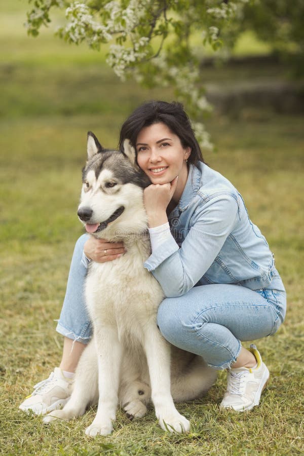 Beautiful brunette girl sitting on the grass with her funny friend malamute dog