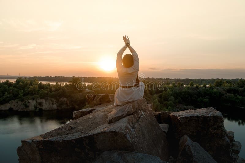 Beautiful brunette girl in a dress meditates at sunset in the mountains, climb the mountains