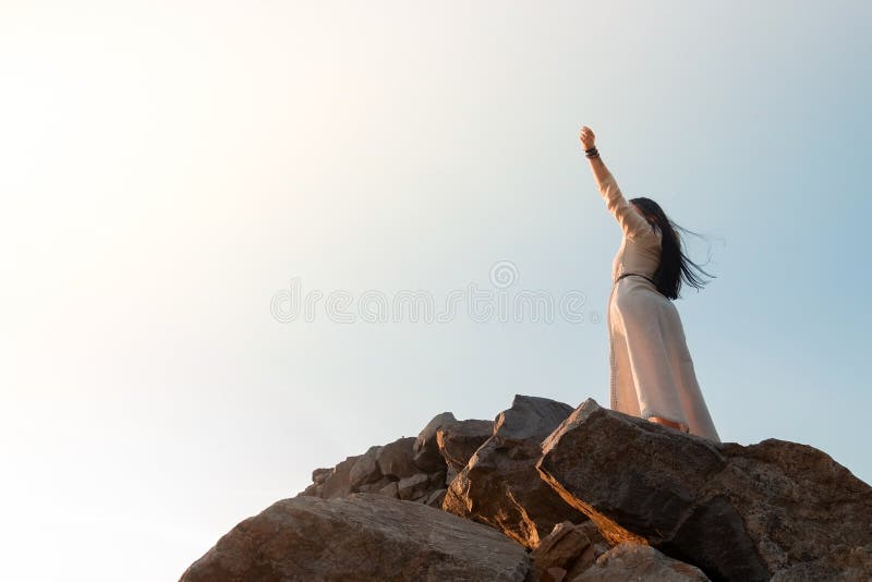 Beautiful brunette girl in a dress meditates at sunset in the mountains, climb the mountains