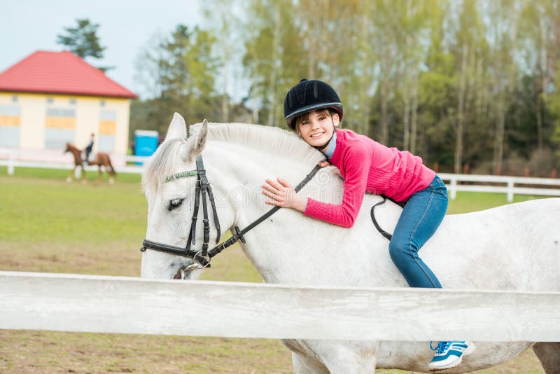 Beautiful brunette girl kissing her horse. A sweet girl riding a white horse, an athlete engaged in equestrian sports. Beautiful brunette girl kissing her horse. A sweet girl riding a white horse, an athlete engaged in equestrian sports