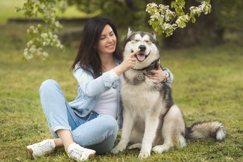 Beautiful brunette girl sitting on the grass with her funny friend malamute dog