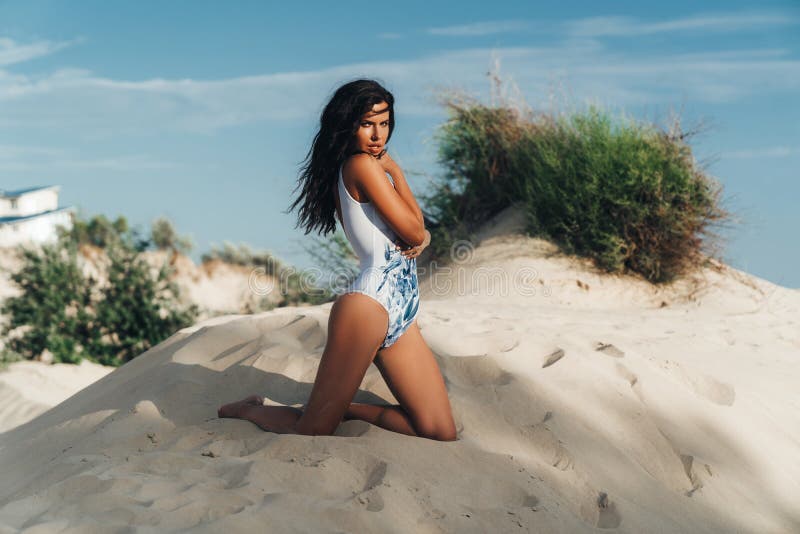 Beautiful brunette girl in a swimsuit resting on the beach near the ocean. Portrait of a young woman with a body