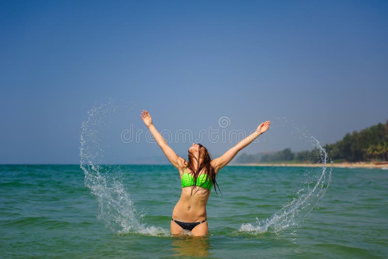Beautiful brunette with long hair stands waist-deep in the ocean and splashes her hands in water. Young slender girl royalty free stock image Beautiful brunette with long hair stands waist-deep in the ocean and splashes her hands in water. Young slender girl royalty free stock image
