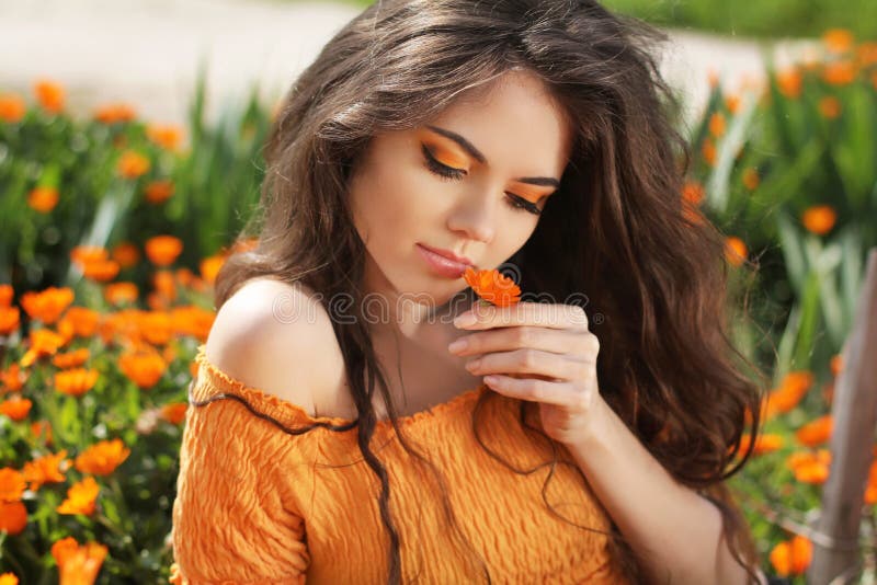Beautiful brunette woman with colored makeup smelling flower, over marigold flowers field