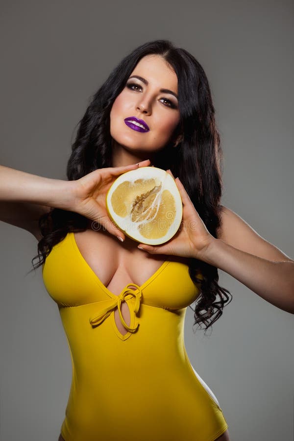 Beautiful brunette woman with perfect body and big breast in yellow swimsuit bikini holding a pomelo citrus fruit royalty free stock image Beautiful brunette woman with perfect body and big breast in yellow swimsuit bikini holding a pomelo citrus fruit royalty free stock image