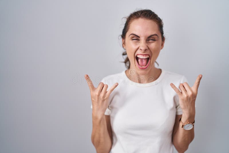 Beautiful brunette woman standing over isolated background shouting with crazy expression doing rock symbol with hands up