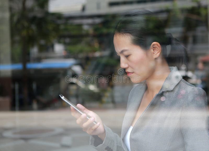 Beautiful business woman using a smartphone at reflection glass of office building