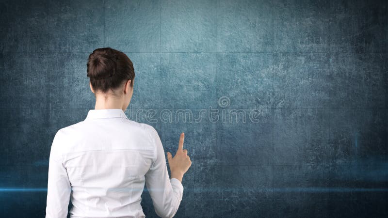 Beautiful business woman in white skirt standing back and pushing an invisible button, isolated studio background.