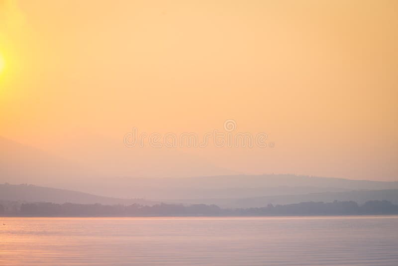 A beautiful, calm morning landscape of lake and mountains in the distance. Colorful summer scenery with mountain lake in dawn.