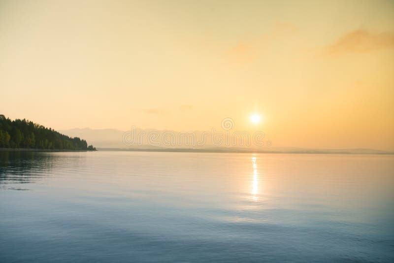 A beautiful, calm morning landscape of lake and mountains in the distance. Colorful summer scenery with mountain lake in dawn.