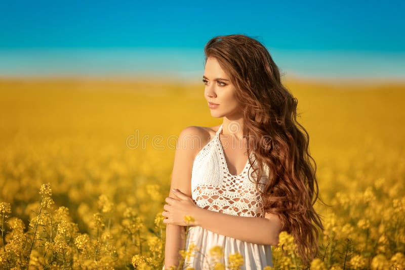 Beautiful carefree girl with long curly healthy hair over Yellow rape field landscape background. Attracive brunette with blowing