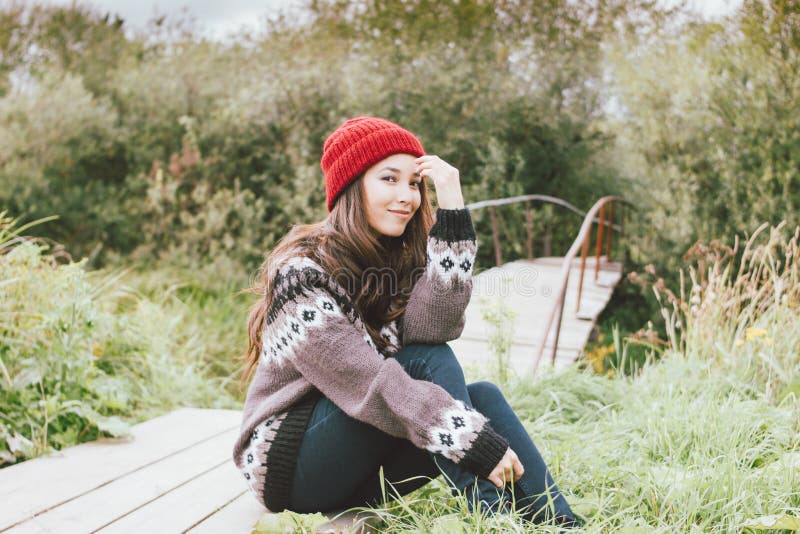 Beautiful carefree long hair asian girl in the red hat and knitted nordic sweater sitting in autumn nature park, travel adventure stock images Beautiful carefree long hair asian girl in the red hat and knitted nordic sweater sitting in autumn nature park, travel adventure stock images