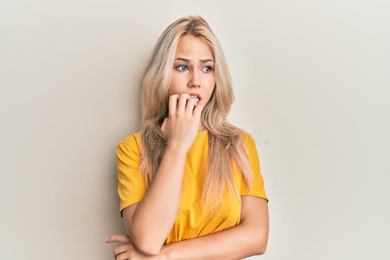 Beautiful caucasian blonde girl wearing casual tshirt looking stressed and nervous with hands on mouth biting nails