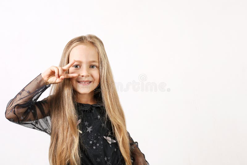 Beautiful caucasian blonde little girl in black dress with stars, white socks and shoes showing V sign victory gesture. Background royalty free stock images Beautiful caucasian blonde little girl in black dress with stars, white socks and shoes showing V sign victory gesture. Background royalty free stock images