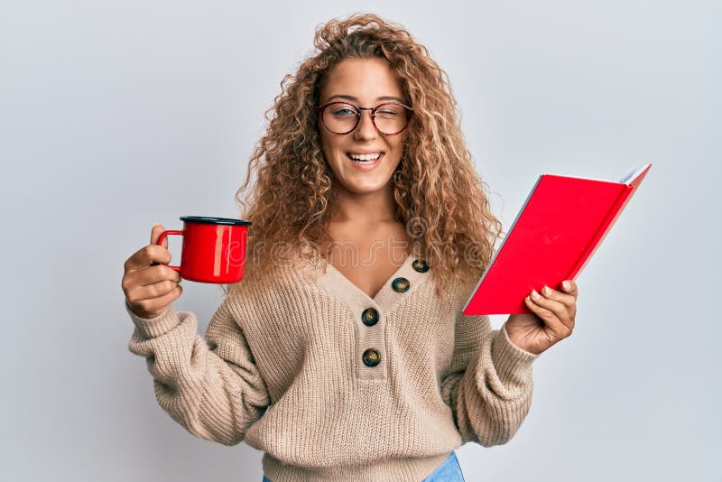 Beautiful caucasian teenager girl reading a book and drinking a cup of coffee winking looking at the camera with sexy expression, cheerful and happy face
