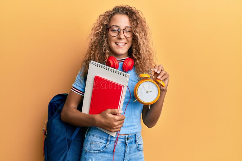 Beautiful caucasian teenager girl wearing student backpack and holding alarm clock winking looking at the camera with sexy expression, cheerful and happy face