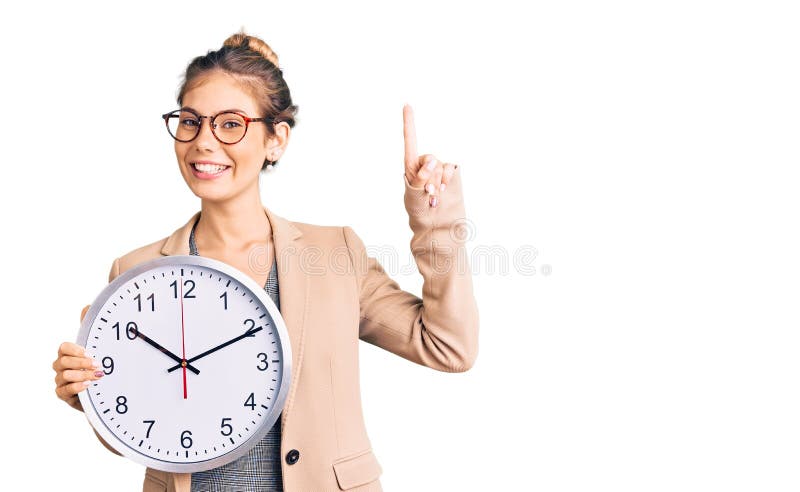 Beautiful caucasian woman with blonde hair wearing business jacket and holding clock surprised with an idea or question pointing