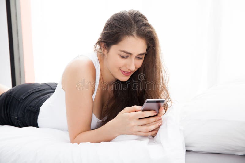 Beautiful Caucasian Woman Laying Down On White Bed Using Mobile Phone And Smile Stock Image