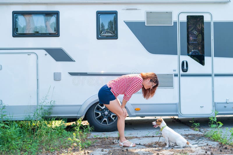 Beautiful caucasian woman is training a dog next to the motorhome. Travel with your pet in a mobile RV. Red-haired girl