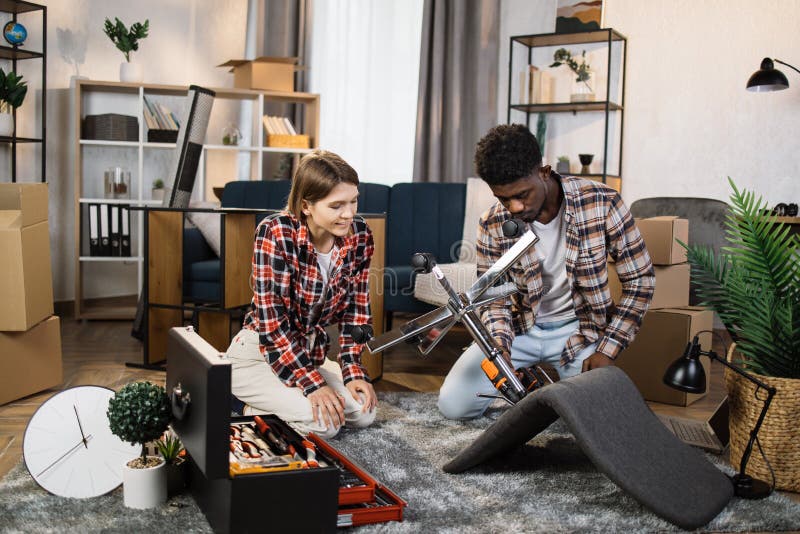 Multiracial young family assembling furniture at new home stock photos