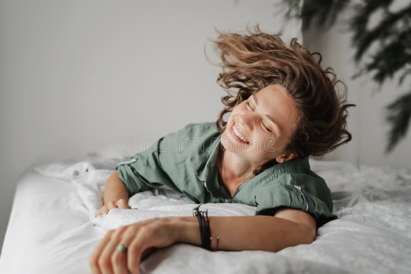 Beautiful charming young curly girl woman in a green shirt lies on the bed, shot of a happy smiling face and flying hair stock images Beautiful charming young curly girl woman in a green shirt lies on the bed, shot of a happy smiling face and flying hair stock images
