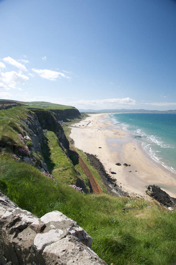 Beach with grassy cliffs and blue sky - Downhill Beach, County Antrim, Ireland. Beach with grassy cliffs and blue sky - Downhill Beach, County Antrim, Ireland.