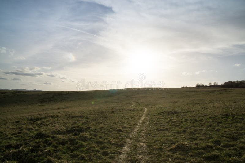 Beautiful clouds over the green meadow, paths and trees, during sunrise or sunset.