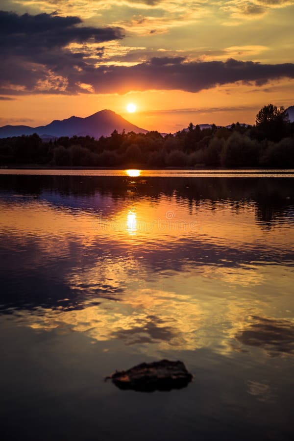 A beautiful, colorful sunset landscape with lake, mountain and forest. Natural evening scenery over the mountain lake in summer.