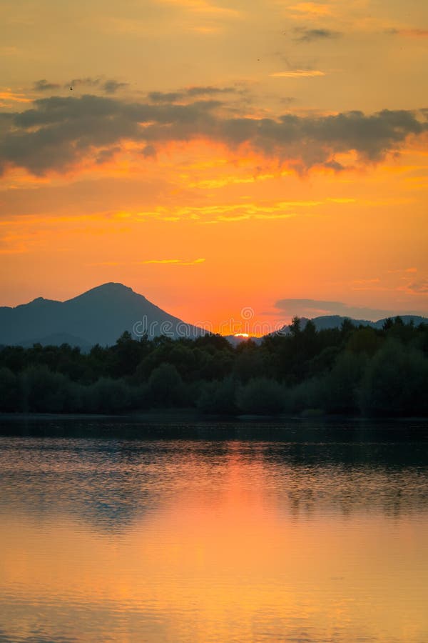 A beautiful, colorful sunset landscape with lake, mountain and forest. Natural evening scenery over the mountain lake in summer.
