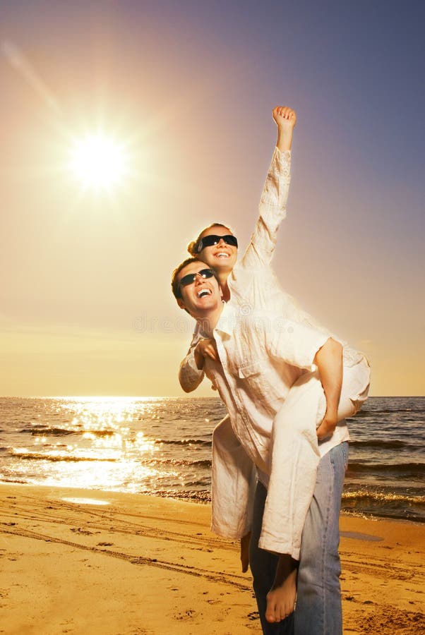 Bel giovane uomo che dà la sua ragazza piggyback ride vicino al mare al tramonto.