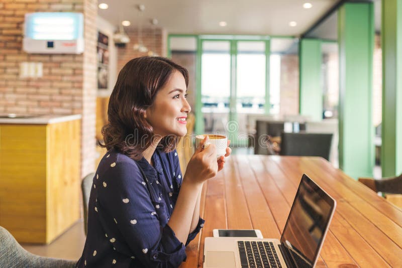 Beautiful cute asian young businesswoman in the cafe, using laptop and drinking coffee smiling royalty free stock images Beautiful cute asian young businesswoman in the cafe, using laptop and drinking coffee smiling royalty free stock images