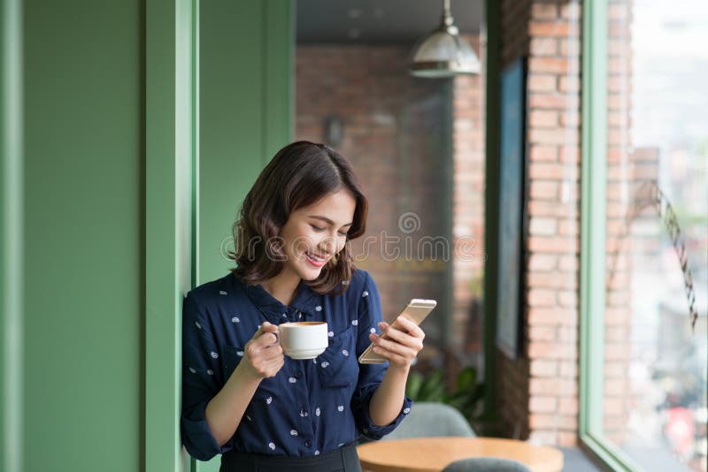 Beautiful cute asian young businesswoman in the cafe, using mobile phone and drinking coffee smiling stock images Beautiful cute asian young businesswoman in the cafe, using mobile phone and drinking coffee smiling stock images