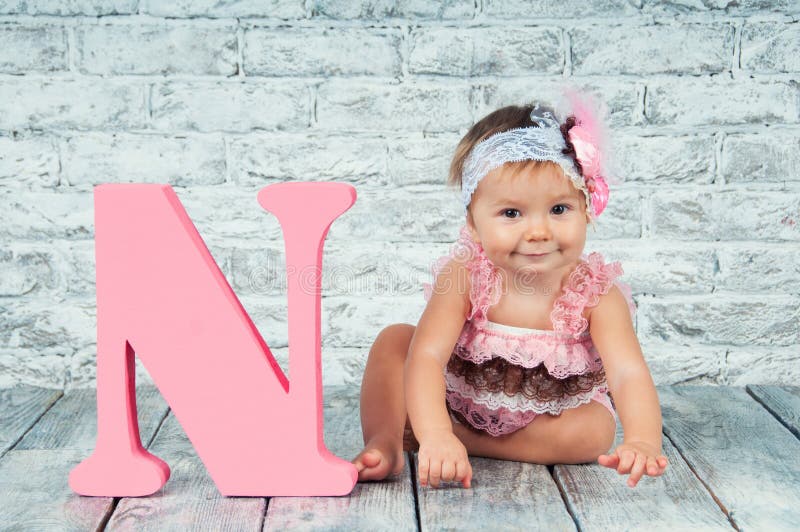 Beautiful and cute girl in pink dress with the letter N. Emotional girl.