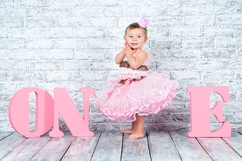 Beautiful and cute girl in a pink dress with the letters one on her first birthday. Emotional girl.