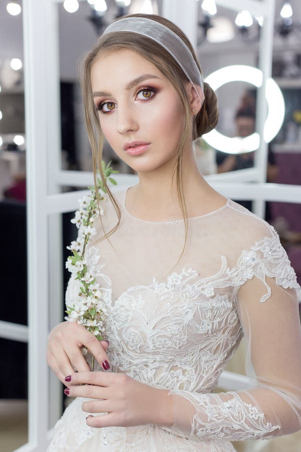 Beautiful cute tender young girl bride in wedding dress in mirrors with evening hair and gentle light make-up