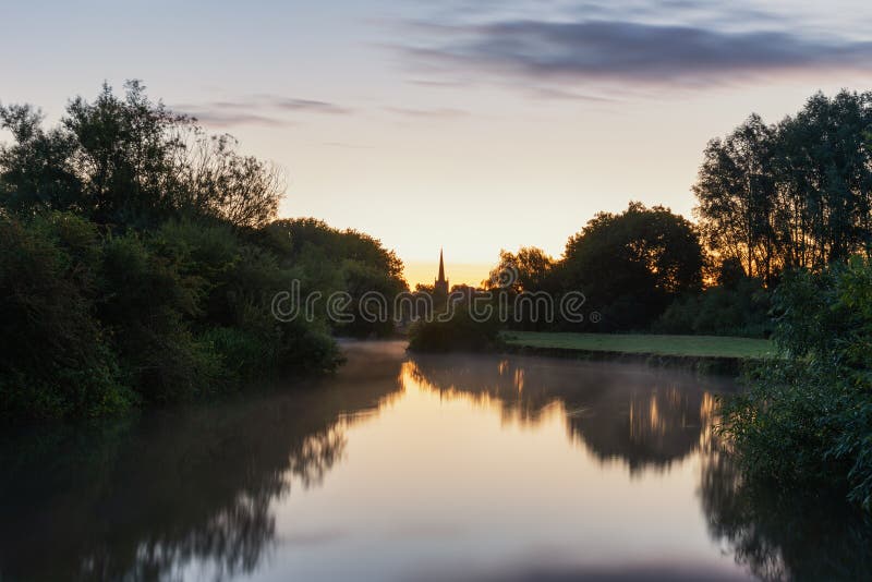 Beautiful dawn landscape image of River Thames at Lechlade-on-Thames in English Cotswolds countryside with church spire in