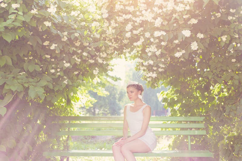 Beautiful delicate elegant woman bride in white dress with hair and tiara on his head sitting in a lush garden on a bench under royalty free stock photos Beautiful delicate elegant woman bride in white dress with hair and tiara on his head sitting in a lush garden on a bench under royalty free stock photos