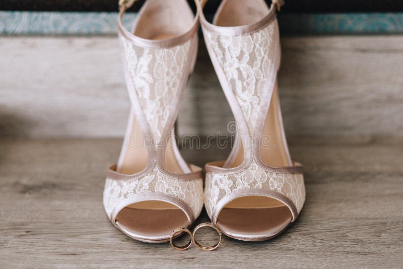 Beautiful designer beige wedding shoes with lace, near gold wedding rings on a parquet stock images Beautiful designer beige wedding shoes with lace, near gold wedding rings on a parquet stock images