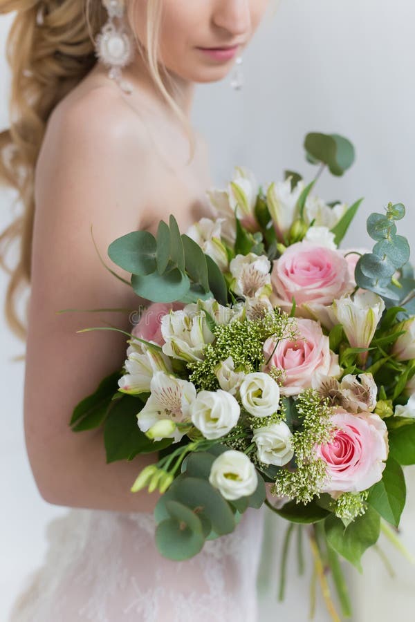 Beautiful elegant bouquet of roses and greenery in the gentle hands of the beautiful bride girl in a pink dress the air