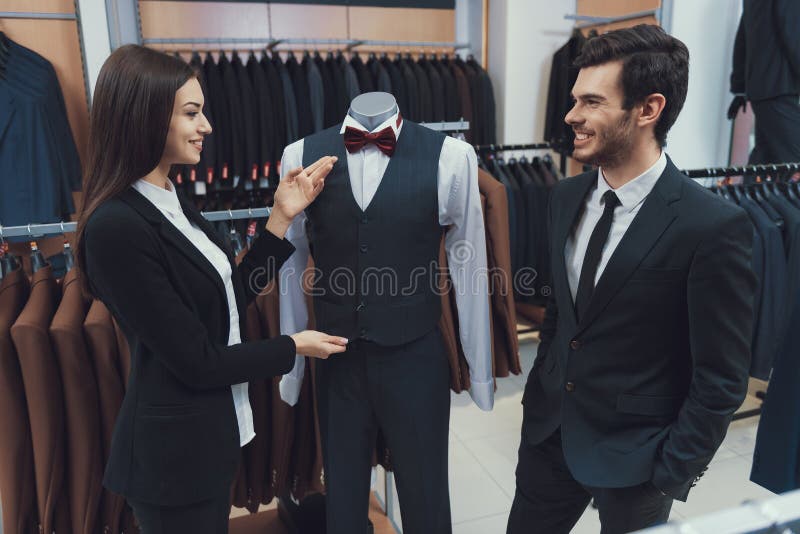 Beautiful elegant girl demonstrates three piece suit on mannequin in men costume store.