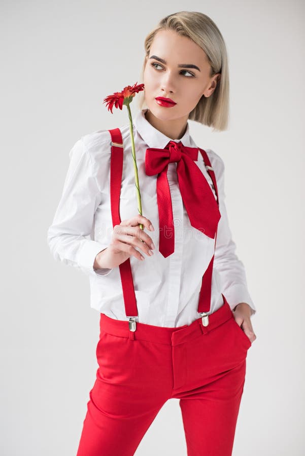 beautiful elegant girl posing in white shirt and red suspenders with red gerbera flower