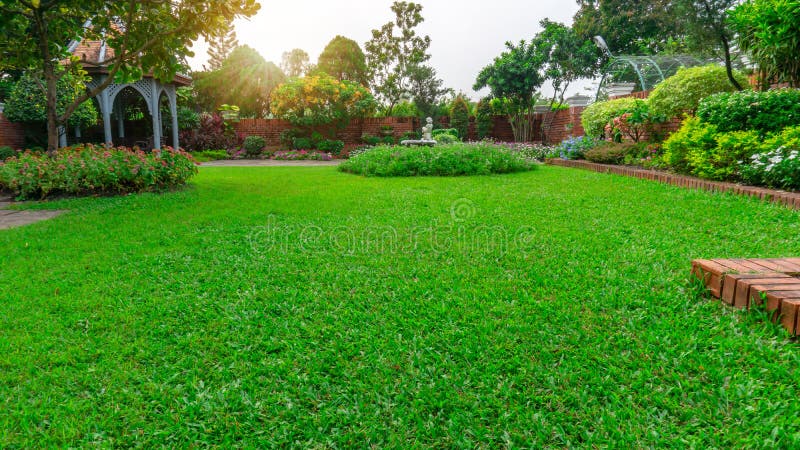 Beautiful English cottage garden, colorful flowering plant on smooth green grass lawn and group of evergreen trees in good care maintenance landscaping of a public park under white sky and sunshine morning. Beautiful English cottage garden, colorful flowering plant on smooth green grass lawn and group of evergreen trees in good care maintenance landscaping of a public park under white sky and sunshine morning